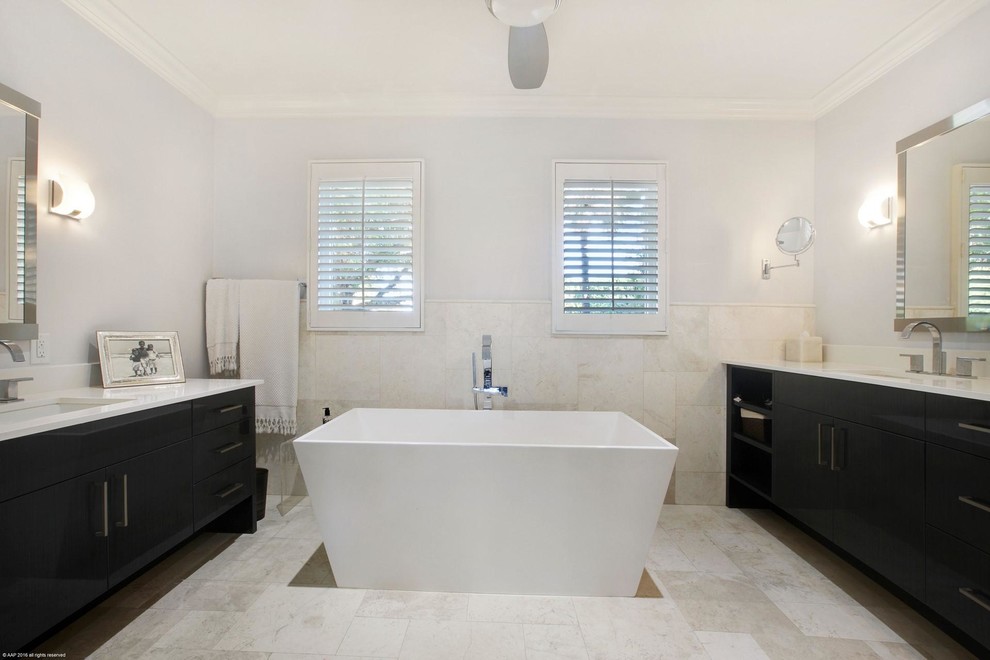Exemple d'une grande salle de bain principale tendance avec un placard à porte plane, des portes de placard noires, une baignoire indépendante, WC à poser, un carrelage beige, des carreaux de céramique, un mur blanc, un sol en travertin, un lavabo encastré et un plan de toilette en marbre.