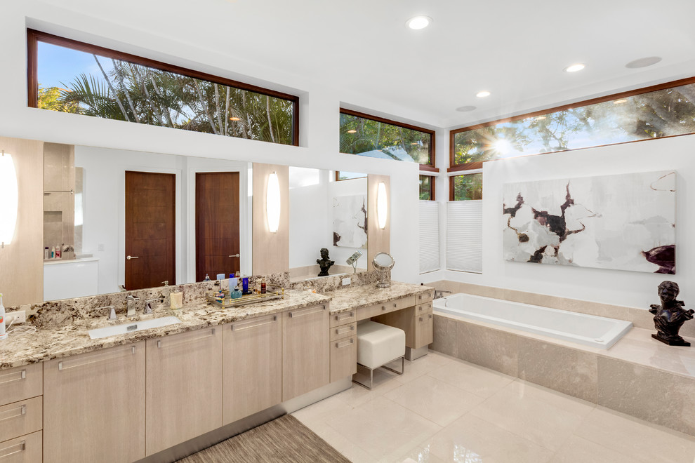 Cette image montre une salle de bain principale design en bois clair avec un placard à porte plane, une baignoire posée, un mur blanc, un lavabo encastré et un sol beige.