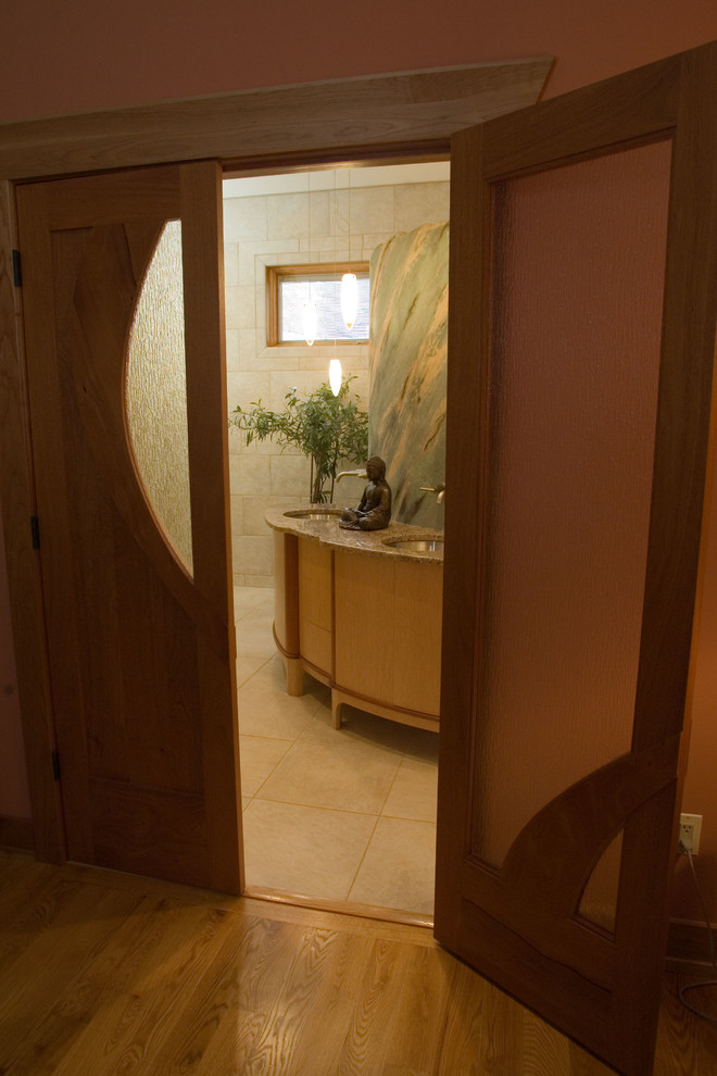 На фото: большая главная ванная комната в стиле фьюжн с врезной раковиной, фасадами островного типа, светлыми деревянными фасадами, столешницей из гранита и бежевой плиткой с