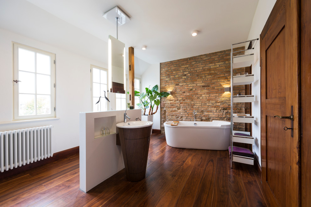 Свежая идея для дизайна: огромная ванная комната в современном стиле с темными деревянными фасадами, отдельно стоящей ванной, белыми стенами, темным паркетным полом, раковиной с пьедесталом и столешницей из дерева - отличное фото интерьера