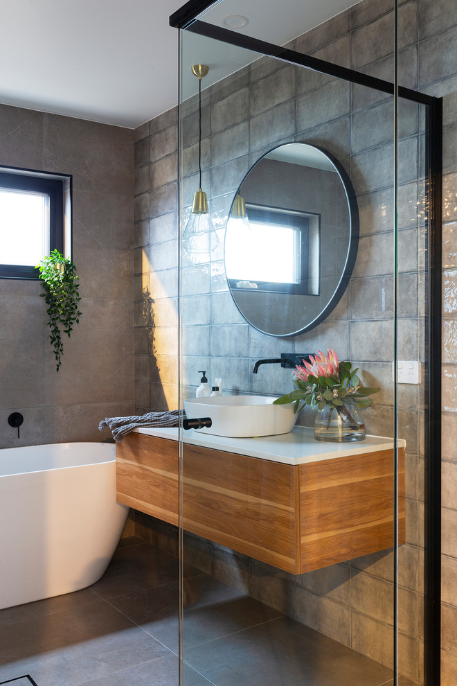 Photo of a medium sized modern ensuite bathroom in Canberra - Queanbeyan with medium wood cabinets, grey tiles, grey walls, porcelain flooring, a vessel sink, engineered stone worktops, a hinged door and white worktops.