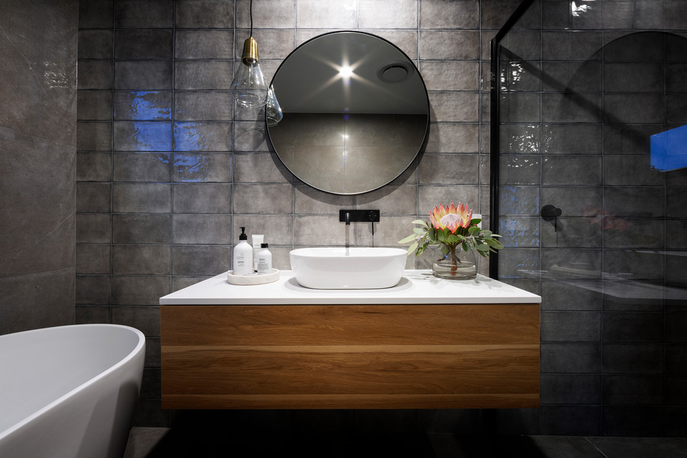 Exemple d'une salle de bain principale moderne en bois brun de taille moyenne avec un carrelage gris, un mur gris, un sol en carrelage de porcelaine, une vasque, un plan de toilette en quartz modifié, une cabine de douche à porte battante et un plan de toilette blanc.