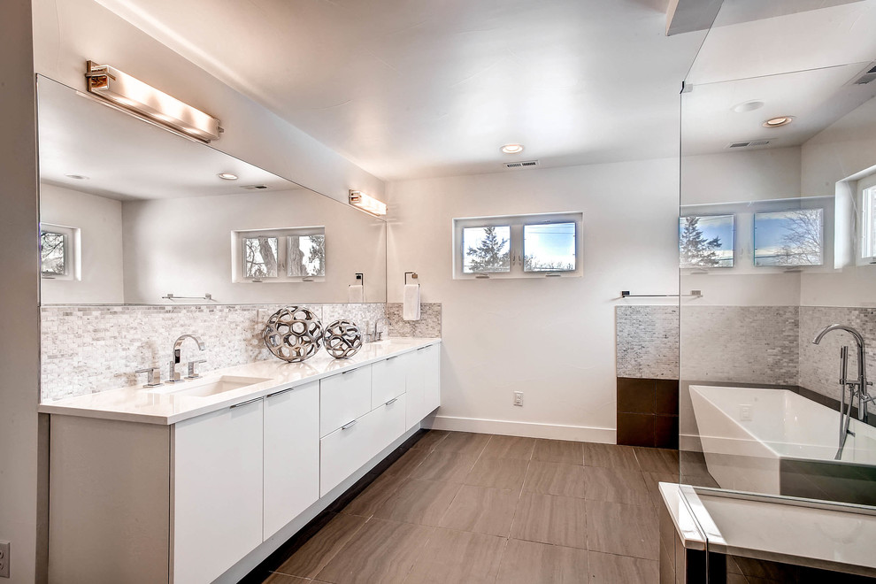 This is an example of a large contemporary ensuite bathroom in Denver with flat-panel cabinets, white cabinets, a freestanding bath, grey tiles, multi-coloured tiles, stone tiles, white walls, a submerged sink, solid surface worktops and a corner shower.