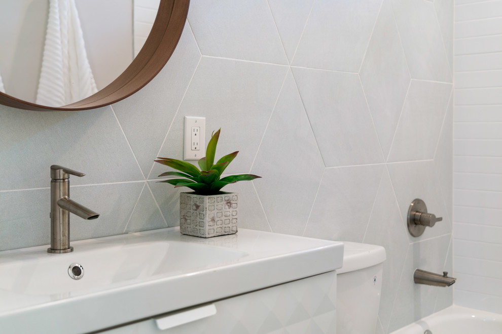 Foto på ett mellanstort vintage vit badrum med dusch, med släta luckor, vita skåp, ett badkar i en alkov, en dusch/badkar-kombination, en toalettstol med separat cisternkåpa, grå kakel, keramikplattor, grå väggar, klinkergolv i keramik, ett integrerad handfat, bänkskiva i akrylsten och svart golv