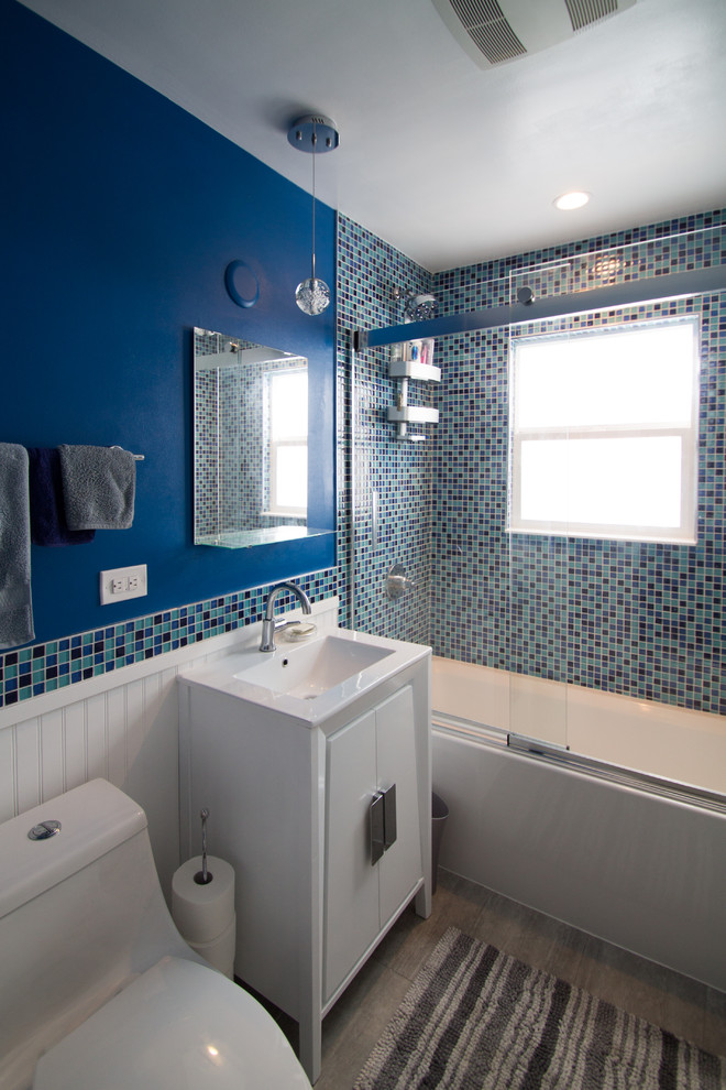 Eklektisk inredning av ett litet en-suite badrum, med släta luckor, vita skåp, ett badkar i en alkov, en dusch/badkar-kombination, en toalettstol med hel cisternkåpa, blå kakel, glaskakel, blå väggar, klinkergolv i porslin, ett undermonterad handfat, bänkskiva i kvarts, grått golv och dusch med skjutdörr