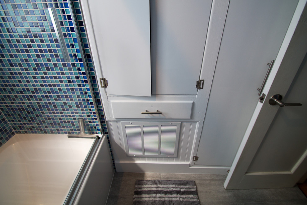 Cette image montre une petite salle de bain principale bohème avec un placard à porte plane, des portes de placard blanches, une baignoire en alcôve, un combiné douche/baignoire, WC à poser, un carrelage bleu, un carrelage en pâte de verre, un mur bleu, un sol en carrelage de porcelaine, un lavabo encastré, un plan de toilette en quartz modifié, un sol gris et une cabine de douche à porte coulissante.