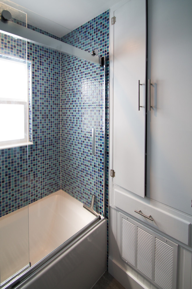 На фото: маленькая главная ванная комната в стиле фьюжн с плоскими фасадами, белыми фасадами, ванной в нише, душем над ванной, унитазом-моноблоком, синей плиткой, стеклянной плиткой, синими стенами, полом из керамогранита, врезной раковиной, столешницей из искусственного кварца, серым полом и душем с раздвижными дверями для на участке и в саду