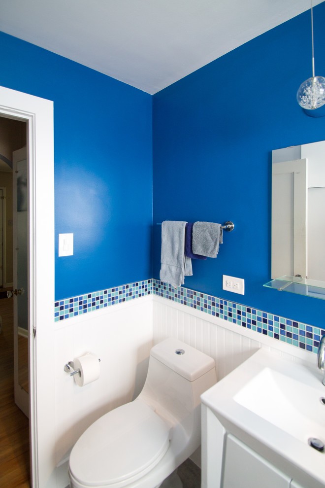 デンバーにある低価格の小さなエクレクティックスタイルのおしゃれなマスターバスルーム (フラットパネル扉のキャビネット、白いキャビネット、アルコーブ型浴槽、シャワー付き浴槽	、一体型トイレ	、青いタイル、ガラスタイル、青い壁、磁器タイルの床、アンダーカウンター洗面器、クオーツストーンの洗面台、グレーの床、引戸のシャワー) の写真