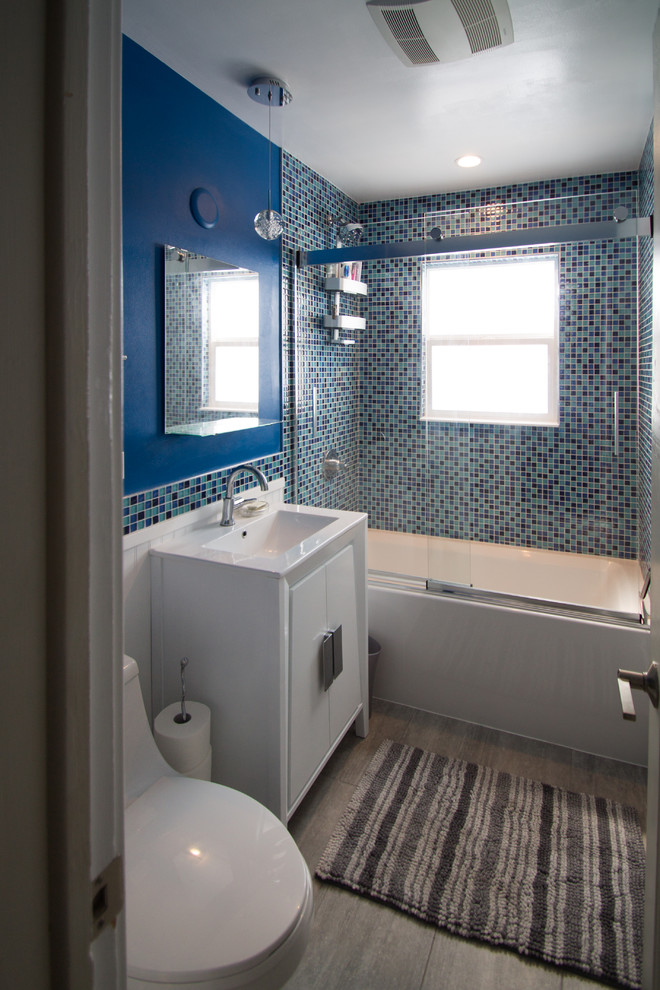 Aménagement d'une petite salle de bain principale éclectique avec un placard à porte plane, des portes de placard blanches, une baignoire en alcôve, un combiné douche/baignoire, WC à poser, un carrelage bleu, un carrelage en pâte de verre, un mur bleu, un sol en carrelage de porcelaine, un lavabo encastré, un plan de toilette en quartz modifié, un sol gris et une cabine de douche à porte coulissante.