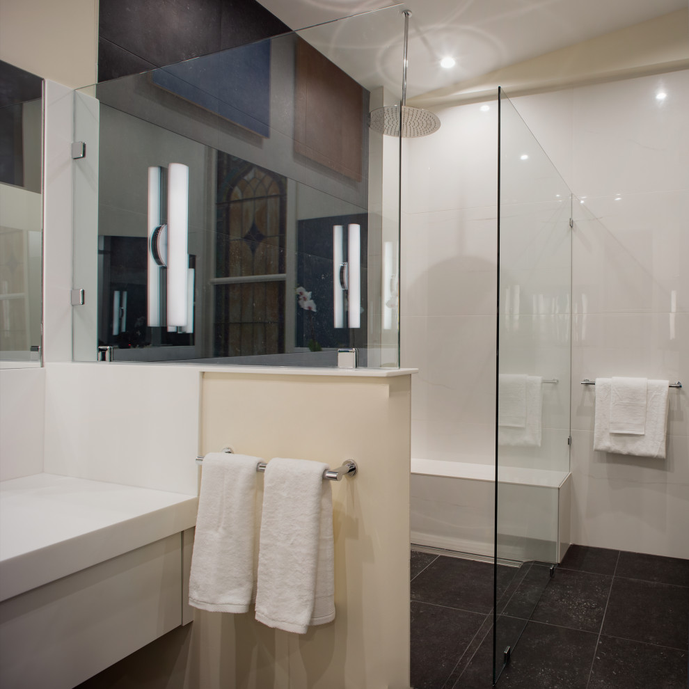 Design ideas for a medium sized contemporary ensuite bathroom in Other with white cabinets, a corner shower, a two-piece toilet, white tiles, ceramic tiles, beige walls, slate flooring, an integrated sink, black floors, a hinged door, white worktops, a shower bench, double sinks, a built in vanity unit and a vaulted ceiling.