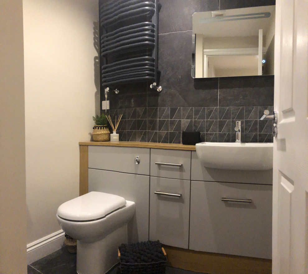 Photo of a small scandi ensuite bathroom in Other with flat-panel cabinets, grey cabinets, a built-in shower, a one-piece toilet, black tiles, porcelain tiles, grey walls, porcelain flooring, a built-in sink, laminate worktops, black floors, a sliding door, beige worktops, a wall niche, a single sink and a built in vanity unit.