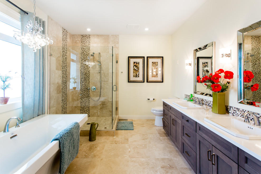 Photo of a large classic ensuite bathroom in Calgary with shaker cabinets, grey cabinets, a freestanding bath, a corner shower, a one-piece toilet, multi-coloured tiles, mosaic tiles, yellow walls, travertine flooring, a built-in sink and engineered stone worktops.