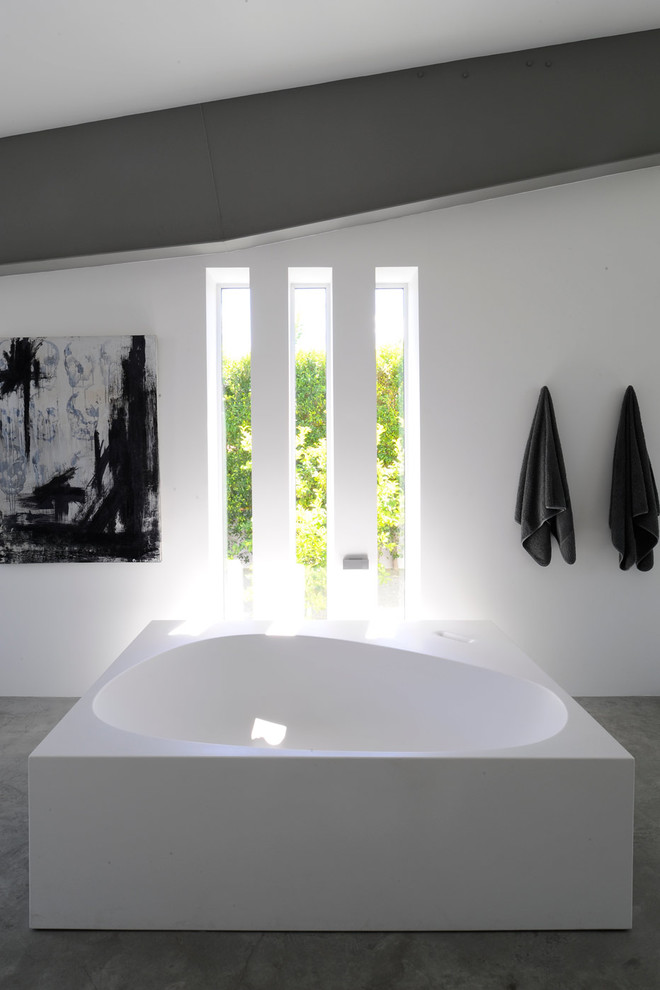 Стильный дизайн: серо-белая ванная комната в современном стиле с отдельно стоящей ванной, белыми стенами и бетонным полом - последний тренд