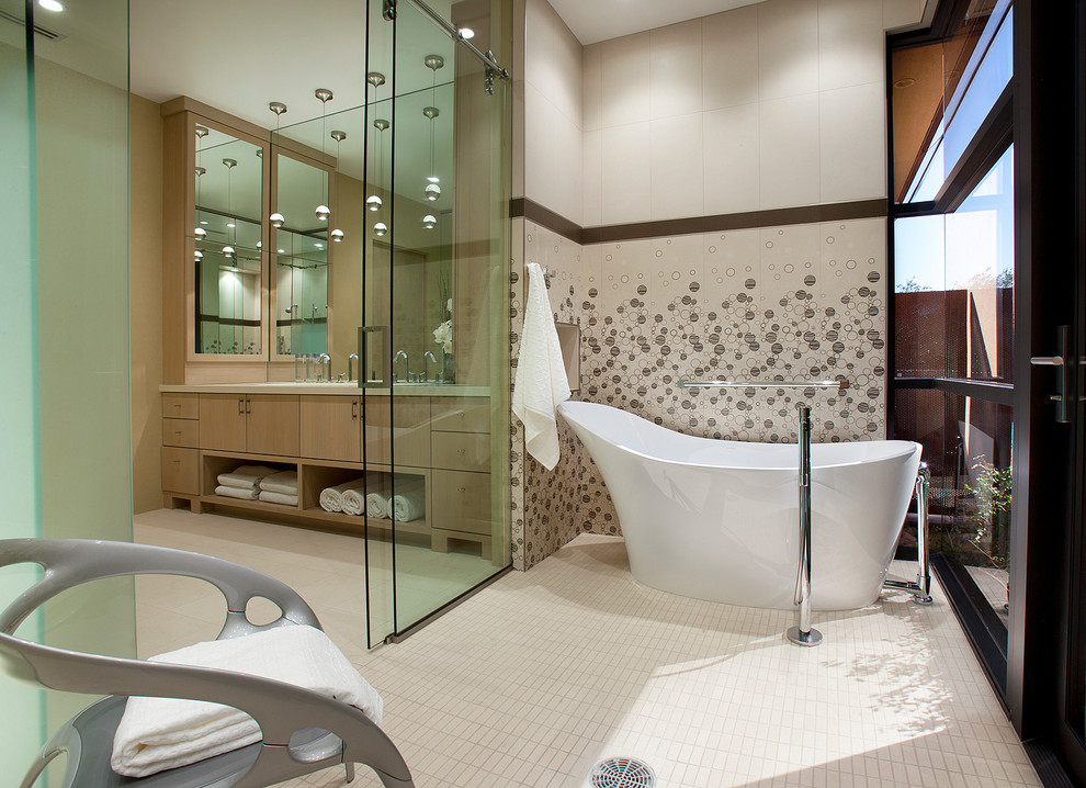 Modelo de cuarto de baño actual con armarios con paneles lisos, puertas de armario de madera clara y bañera exenta