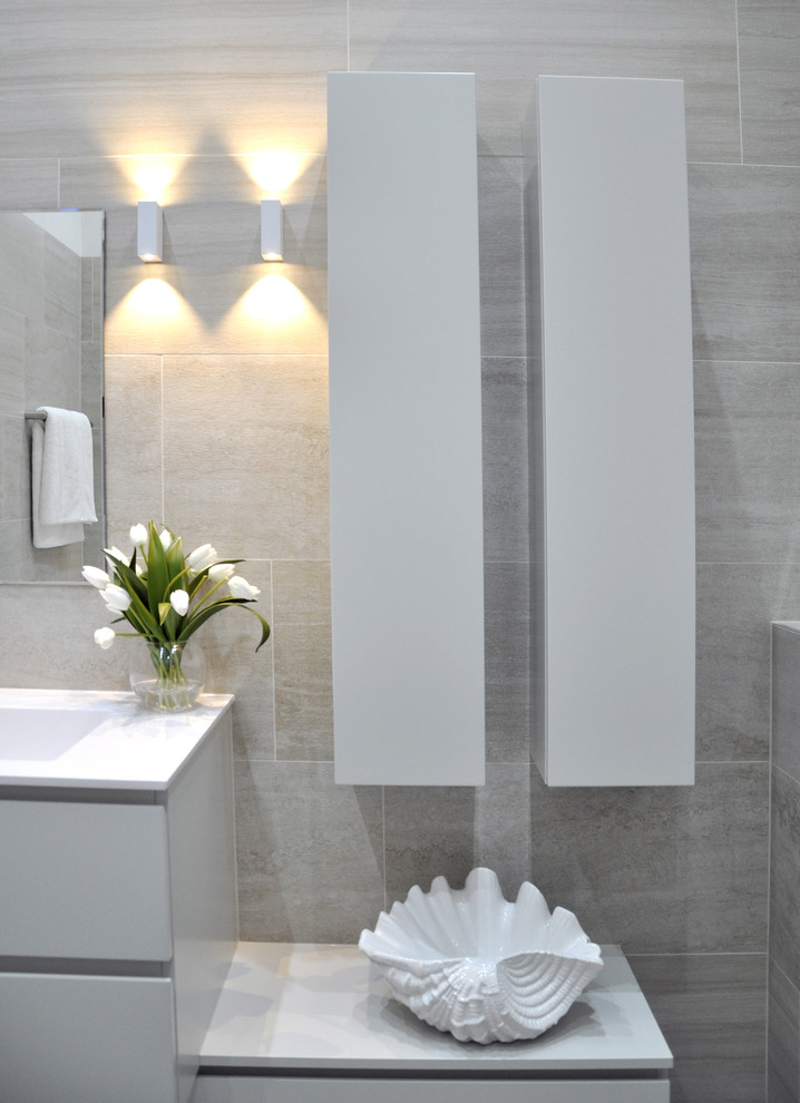 Idéer för att renovera ett mellanstort funkis en-suite badrum, med ett nedsänkt handfat, släta luckor, grå skåp, bänkskiva i akrylsten, ett platsbyggt badkar, en dusch/badkar-kombination, en vägghängd toalettstol, beige kakel, keramikplattor, vita väggar och klinkergolv i keramik