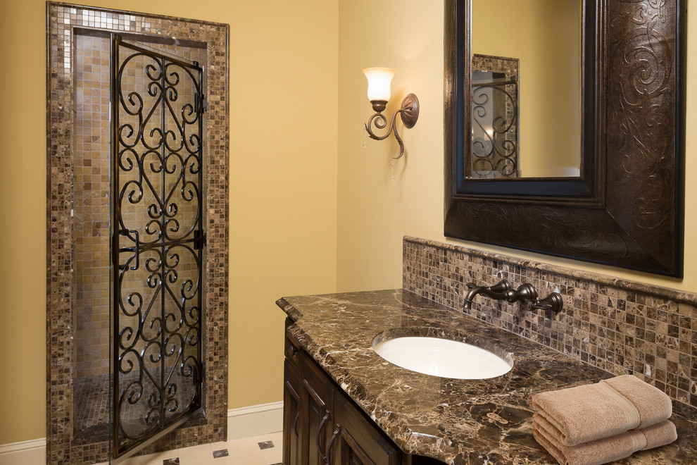 This is an example of a medium sized mediterranean bathroom in Kansas City with dark wood cabinets, brown tiles, mosaic tiles, ceramic flooring, a submerged sink, raised-panel cabinets, marble worktops, an alcove shower and yellow walls.
