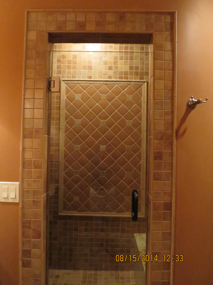 Cette image montre une douche en alcôve méditerranéenne en bois foncé de taille moyenne avec un plan de toilette en granite, un carrelage marron, mosaïque, un sol en carrelage de céramique, un lavabo encastré, un mur orange et un placard avec porte à panneau surélevé.