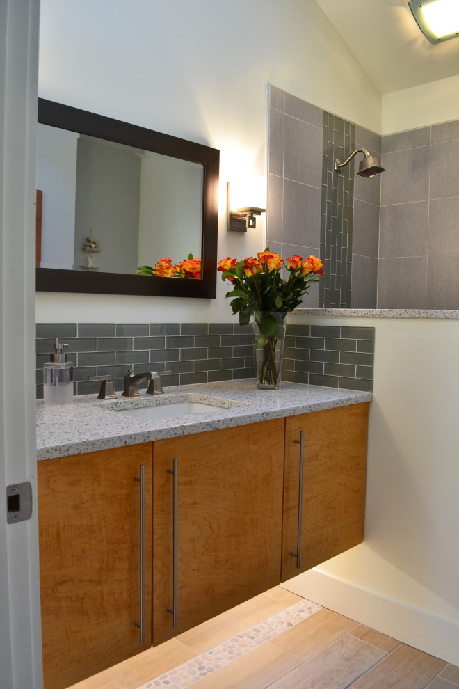 Пример оригинального дизайна: маленькая ванная комната в современном стиле с плоскими фасадами, фасадами цвета дерева среднего тона, угловым душем, раздельным унитазом, серой плиткой, стеклянной плиткой, белыми стенами, полом из керамогранита, душевой кабиной, врезной раковиной, столешницей из переработанного стекла, бежевым полом, душем с распашными дверями и разноцветной столешницей для на участке и в саду