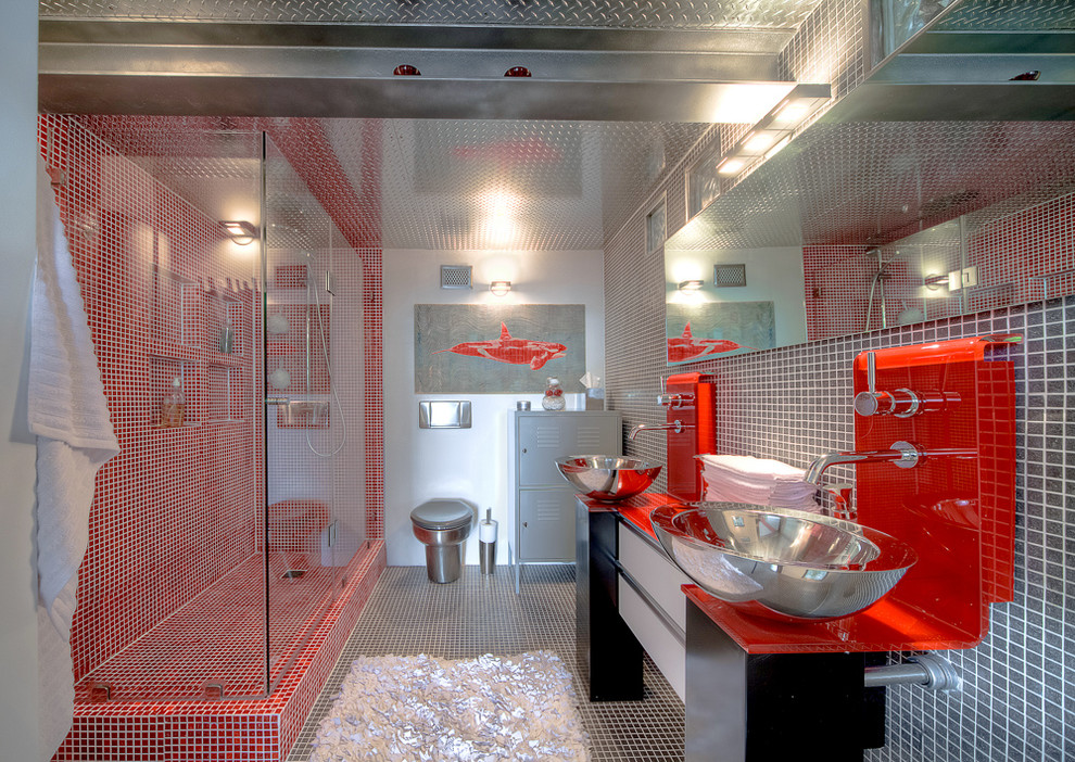Inredning av ett industriellt badrum med dusch, med släta luckor, svarta skåp, en hörndusch, en toalettstol med hel cisternkåpa, röd kakel, ett fristående handfat och dusch med gångjärnsdörr