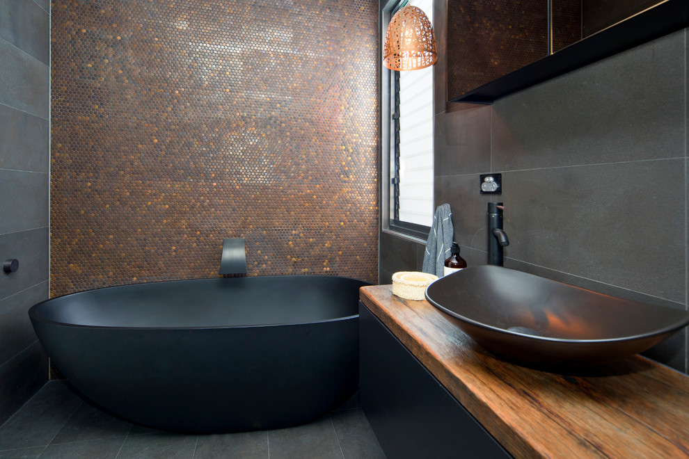 Idéer för ett modernt en-suite badrum, med släta luckor, svarta skåp, ett fristående badkar, svart kakel, porslinskakel, svarta väggar, klinkergolv i porslin, ett fristående handfat, träbänkskiva och svart golv