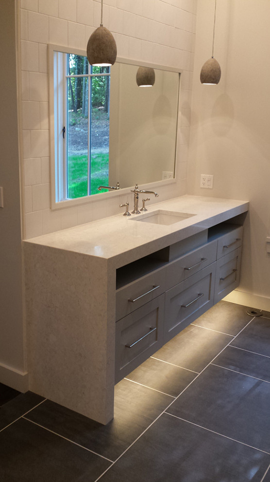 Exemple d'une salle de bain tendance avec un placard à porte shaker, des portes de placard grises, un carrelage blanc, un mur blanc, un lavabo encastré, un sol noir et un plan de toilette blanc.