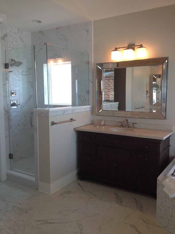 Immagine di una stanza da bagno padronale costiera con lavabo sottopiano, ante con bugna sagomata, ante in legno bruno, top in marmo, doccia ad angolo, piastrelle beige, piastrelle in pietra, pareti beige e pavimento in marmo