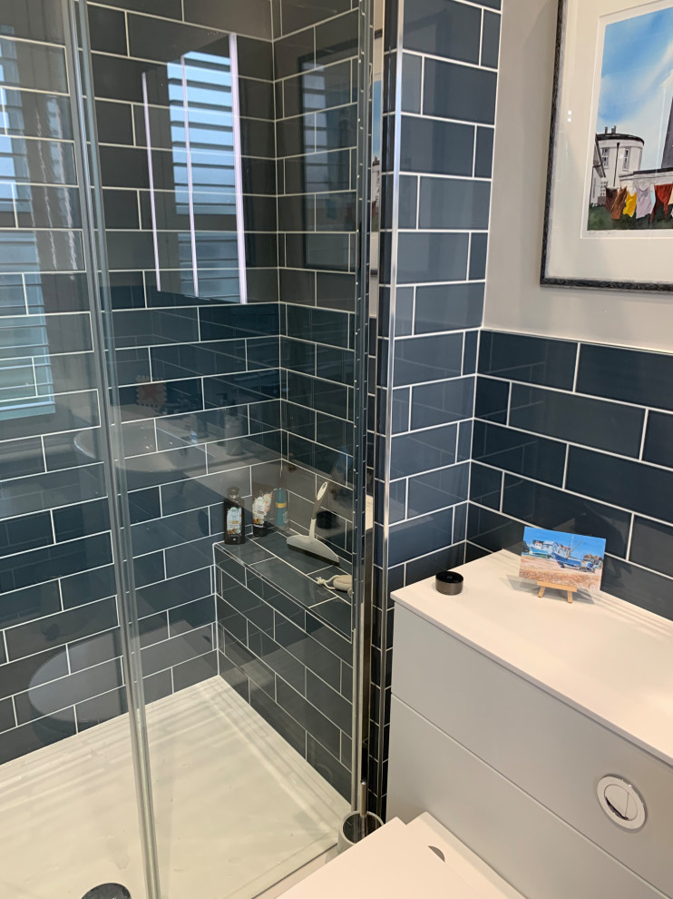 Inspiration for a small modern ensuite bathroom in Sussex with flat-panel cabinets, white cabinets, an alcove shower, a wall mounted toilet, blue tiles, metro tiles, blue walls, vinyl flooring, an integrated sink, marble worktops, beige floors, a sliding door, white worktops, a single sink and a built in vanity unit.