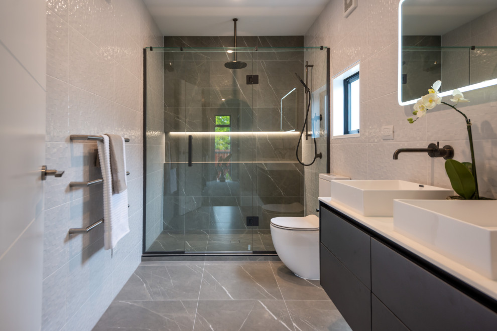 Modern inredning av ett mellanstort vit vitt en-suite badrum, med svarta skåp, ett fristående badkar, en dusch i en alkov, svart och vit kakel, keramikplattor, grå väggar, klinkergolv i keramik, ett fristående handfat, bänkskiva i kvarts och släta luckor