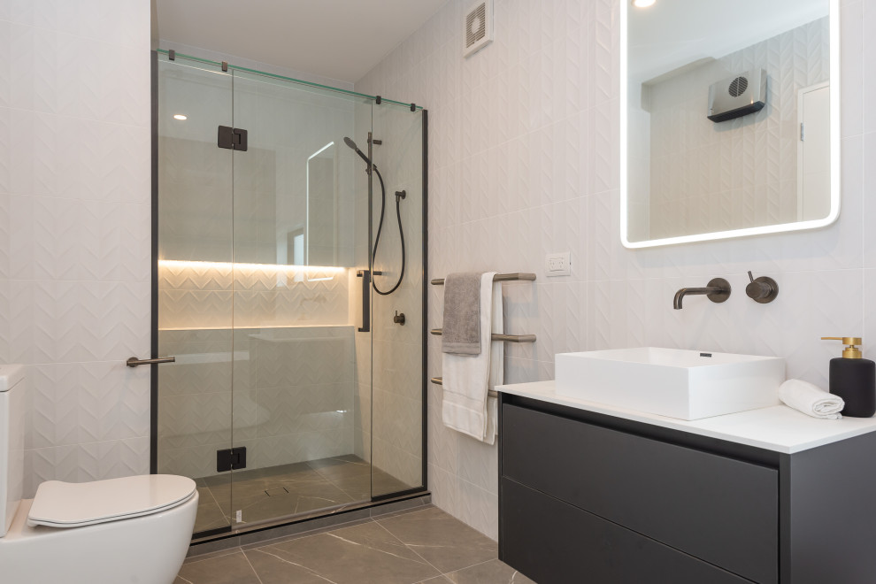 Design ideas for a medium sized modern ensuite bathroom in Christchurch with freestanding cabinets, black cabinets, a freestanding bath, an alcove shower, black and white tiles, ceramic tiles, grey walls, ceramic flooring, a vessel sink, engineered stone worktops, white worktops, a single sink and a floating vanity unit.