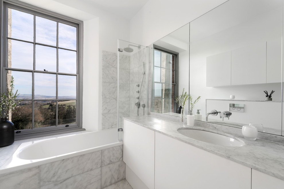 Idéer för att renovera ett mellanstort funkis en-suite badrum, med släta luckor, vita skåp, ett platsbyggt badkar, en kantlös dusch, en vägghängd toalettstol, vit kakel, stenhäll, vita väggar, marmorgolv, ett nedsänkt handfat, marmorbänkskiva, vitt golv och med dusch som är öppen