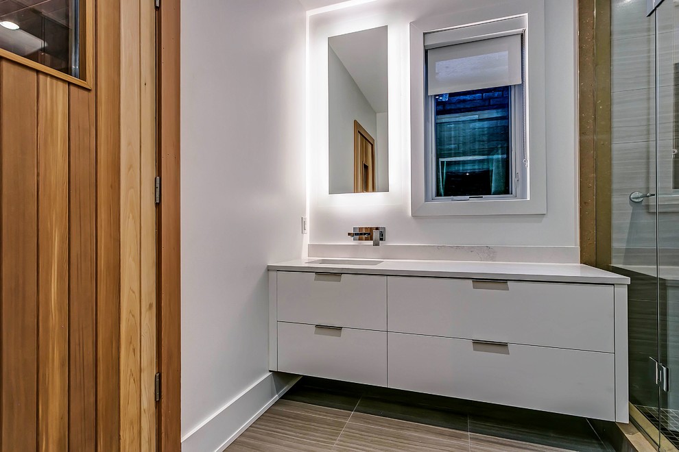 Inredning av ett minimalistiskt badrum, med släta luckor, vita skåp, vita väggar, ett undermonterad handfat och bänkskiva i kvarts