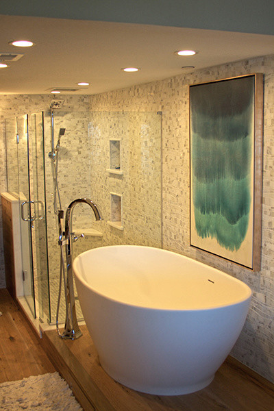 Cette image montre une grande salle de bain principale marine avec une baignoire indépendante, une douche d'angle, un mur gris et un sol en bois brun.