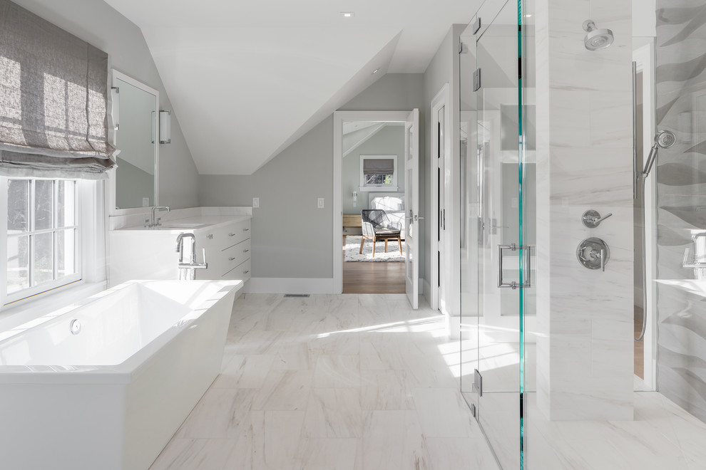 Inspiration for a large beach style ensuite bathroom in Boston with flat-panel cabinets, white cabinets, a freestanding bath, a built-in shower, white tiles, stone tiles, grey walls, marble flooring, a submerged sink and marble worktops.