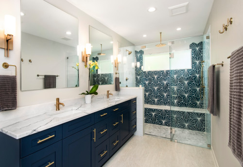 Contemporary bathroom with navy blue bathroom cabinets, marble countertop, brass hardware, and glass shower with geometric tile wall.