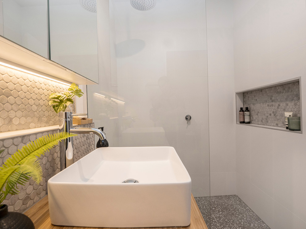 Cette image montre une petite salle de bain design avec des portes de placard blanches, un carrelage blanc, des carreaux de céramique, un mur blanc, un sol en terrazzo, un plan de toilette en bois et aucune cabine.