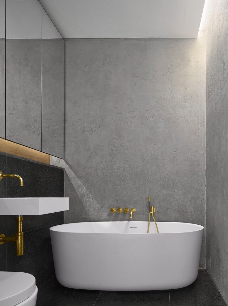 Пример оригинального дизайна: ванная комната в современном стиле с отдельно стоящей ванной, черной плиткой, серыми стенами, подвесной раковиной и черным полом