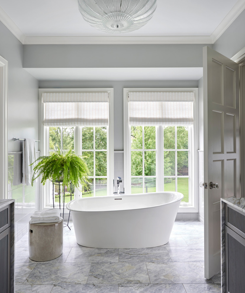 Klassisk inredning av ett grå grått badrum, med ett fristående badkar, grå kakel, grå väggar och grått golv