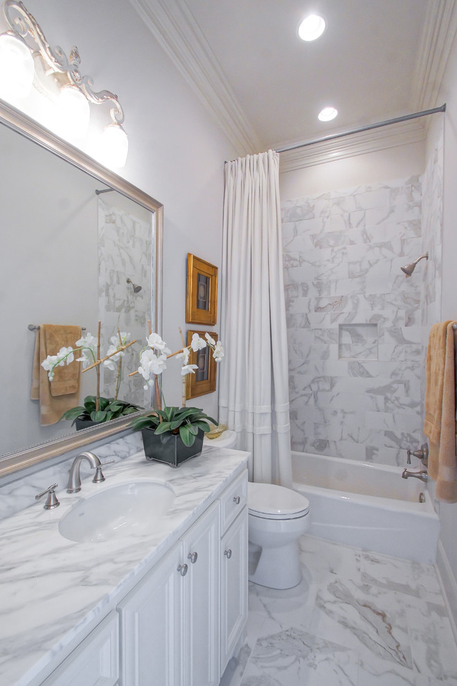 Idéer för ett mellanstort klassiskt badrum, med ett undermonterad handfat, luckor med upphöjd panel, vita skåp, marmorbänkskiva, ett badkar i en alkov, en dusch/badkar-kombination, en toalettstol med hel cisternkåpa, vit kakel, porslinskakel, vita väggar och klinkergolv i porslin