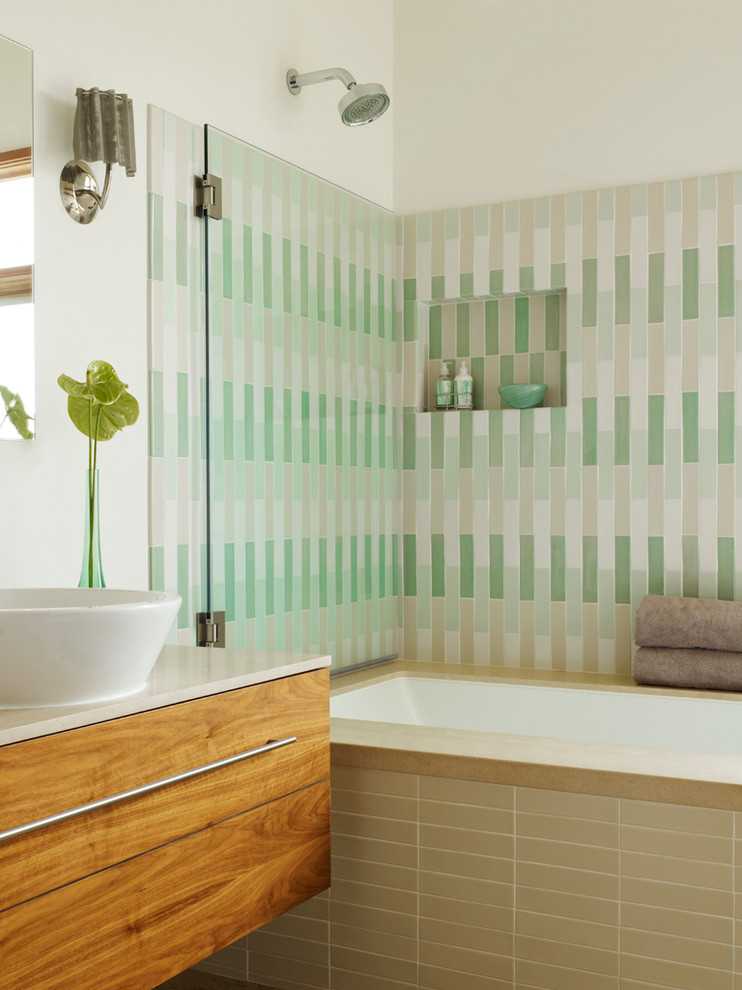 Cette photo montre une salle de bain moderne en bois brun avec un combiné douche/baignoire, une vasque, un placard à porte plane, mosaïque, un mur blanc et un plan de toilette en calcaire.