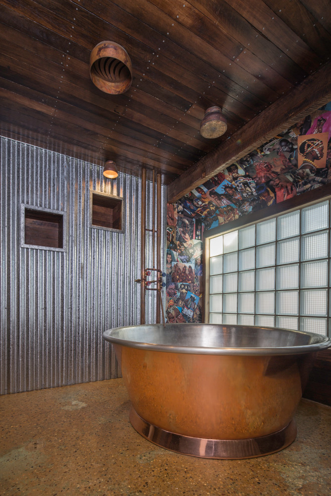 Cette image montre une salle de bain urbaine avec une baignoire indépendante, un mur gris, sol en béton ciré et un sol marron.