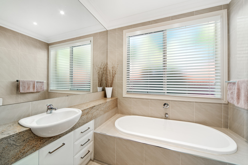 Exempel på ett modernt badrum, med möbel-liknande, vita skåp, ett platsbyggt badkar, beige kakel, ett integrerad handfat och granitbänkskiva