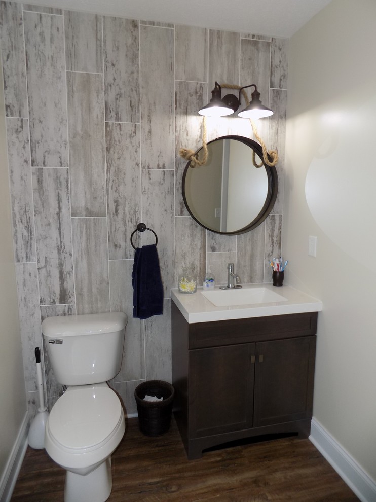 Small beach style 3/4 beige tile and ceramic tile medium tone wood floor and brown floor drop-in bathtub photo in Columbus with recessed-panel cabinets, dark wood cabinets, a two-piece toilet, beige walls, an integrated sink and solid surface countertops