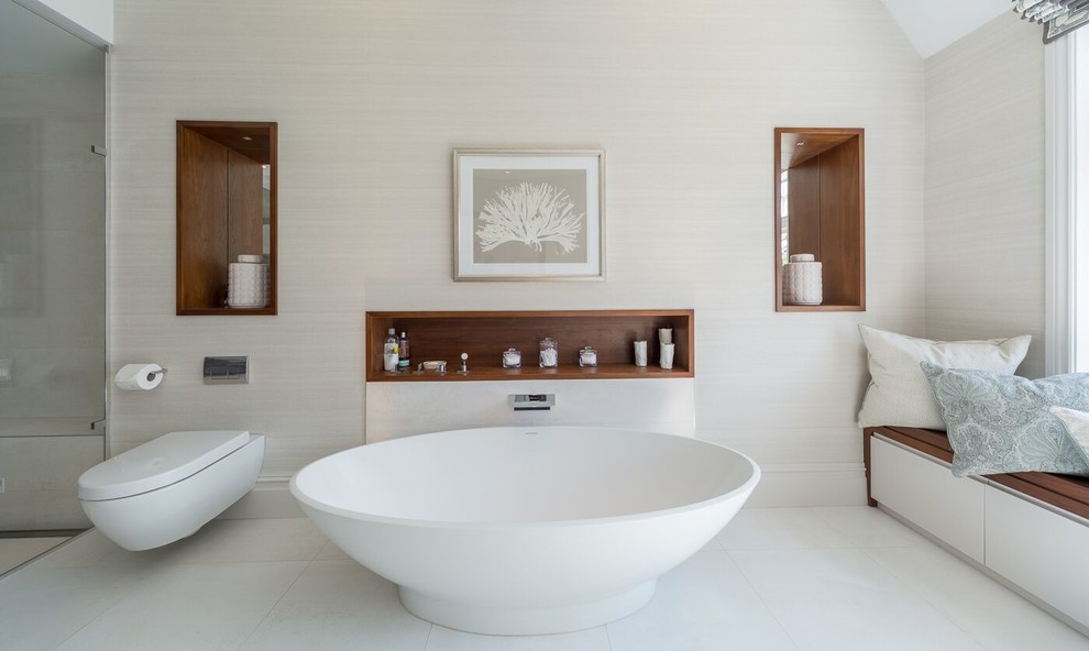 Inspiration för ett funkis en-suite badrum, med släta luckor, vita skåp, ett fristående badkar, en kantlös dusch, en vägghängd toalettstol och beige väggar