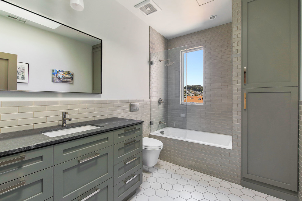Inspiration for a traditional bathroom in San Francisco with shaker cabinets, grey cabinets, a shower/bath combination, a wall mounted toilet, grey tiles, porcelain flooring, a submerged sink, soapstone worktops, white floors and an open shower.