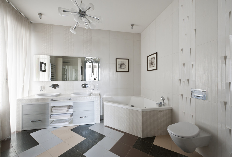Imagen de cuarto de baño principal actual grande con armarios con paneles lisos, puertas de armario blancas, bañera esquinera, sanitario de pared, paredes blancas y lavabo encastrado