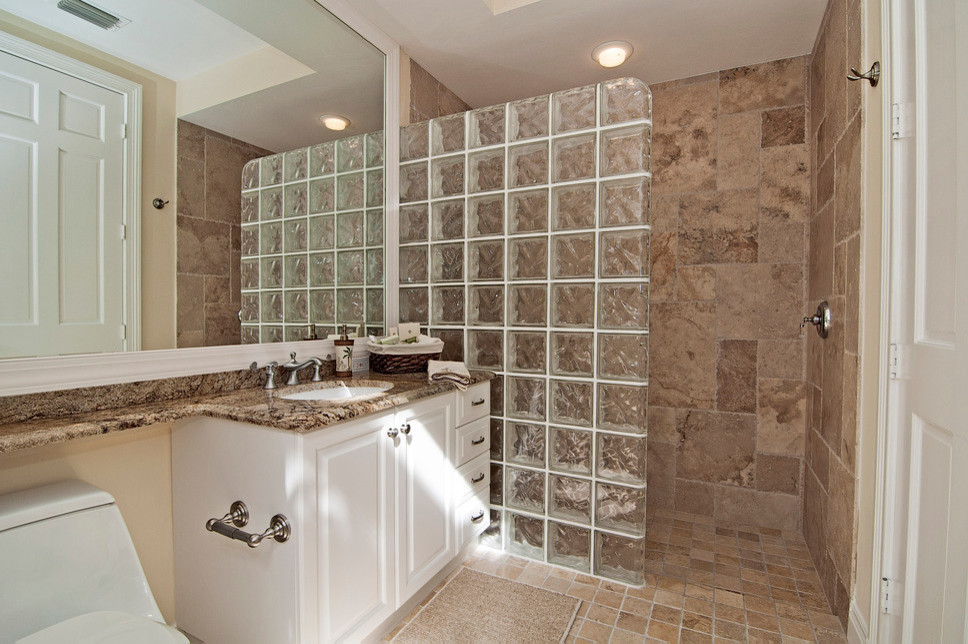 Inredning av ett modernt mellanstort en-suite badrum, med ett undermonterad handfat, luckor med upphöjd panel, vita skåp, bänkskiva i akrylsten, en öppen dusch, en toalettstol med hel cisternkåpa, brun kakel, stenkakel, beige väggar och travertin golv