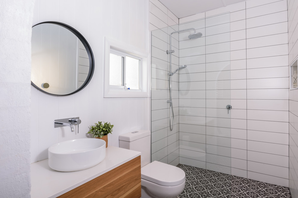 Inredning av ett modernt litet badrum, med släta luckor, skåp i mellenmörkt trä, vit kakel, keramikplattor, vita väggar, klinkergolv i keramik, flerfärgat golv och med dusch som är öppen