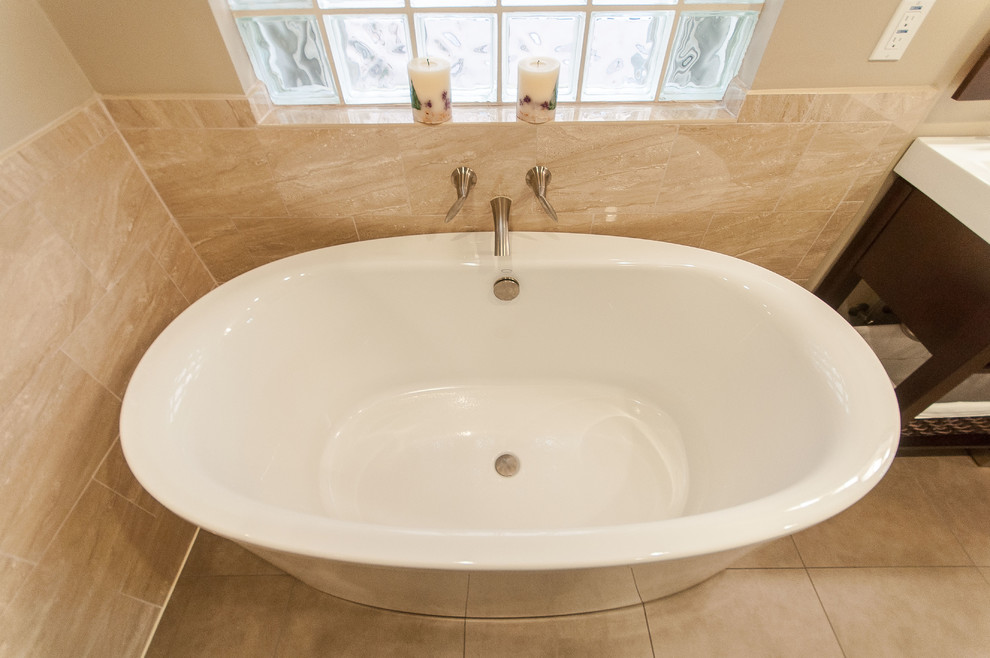 Inredning av ett klassiskt badrum, med släta luckor, bruna skåp, bänkskiva i kvarts, ett fristående badkar, en dusch i en alkov, en toalettstol med separat cisternkåpa, beige kakel och porslinskakel