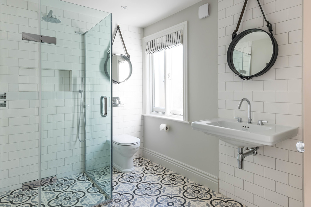 Foto på ett lantligt badrum, med en hörndusch, en toalettstol med hel cisternkåpa, vit kakel, tunnelbanekakel, grå väggar, ett väggmonterat handfat, cementgolv och dusch med gångjärnsdörr