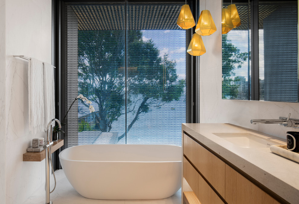 Стильный дизайн: ванная комната в современном стиле с плоскими фасадами, отдельно стоящей ванной, белой плиткой, белыми стенами, накладной раковиной, белым полом, бежевой столешницей и фасадами цвета дерева среднего тона - последний тренд